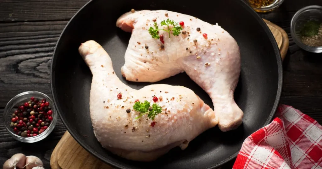 Raw chicken thighs marinated in a flavorful blend of spices, herbs, and oil in a glass bowl, ready for grilling or baking