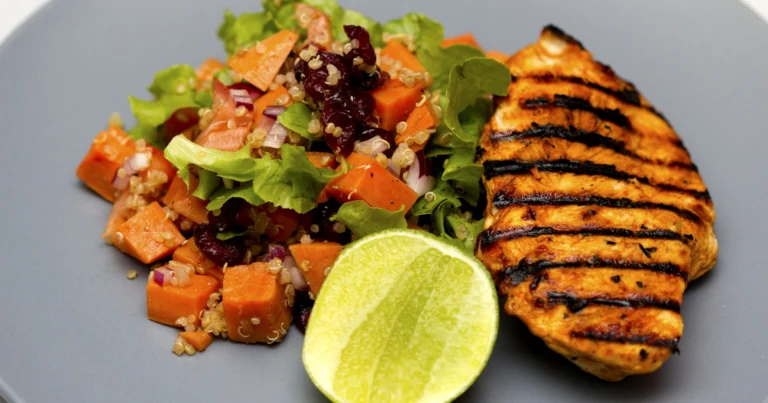 Golden-brown roasted split chicken breast served on a plate with fresh herbs and roasted vegetables.